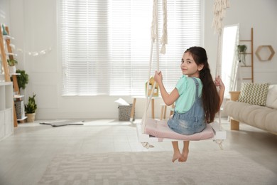 Cute little girl playing on swing at home. Space for text