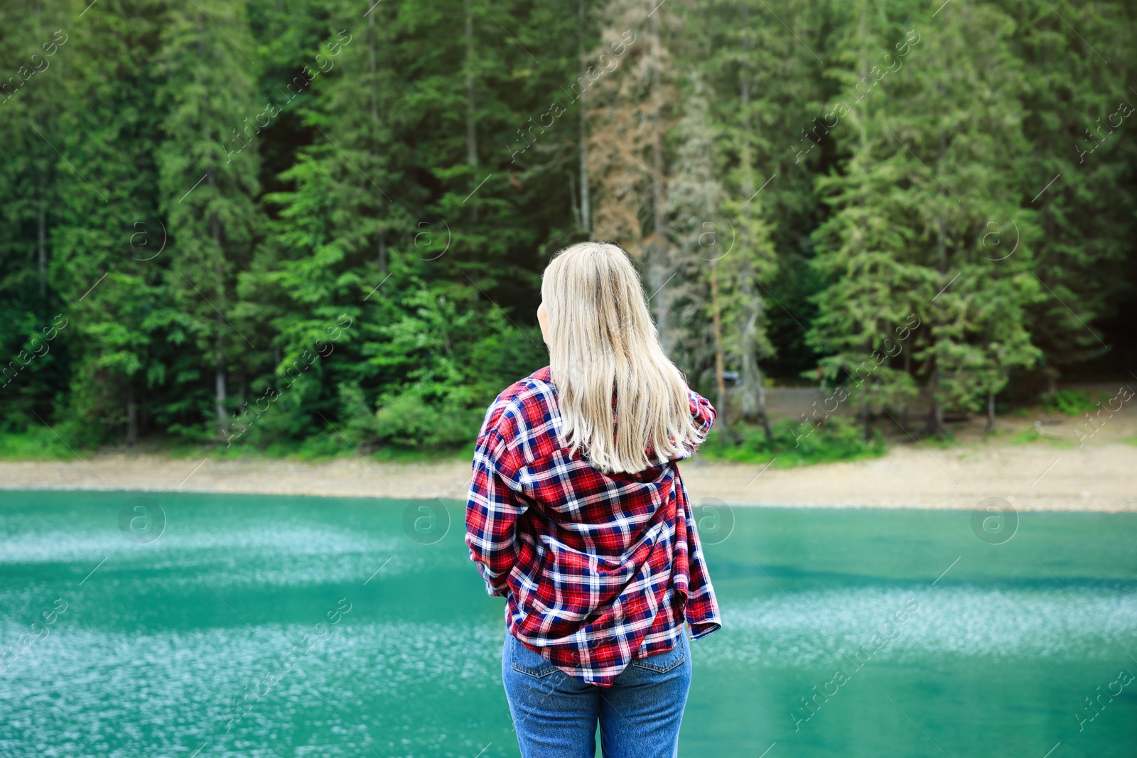 Photo of Woman near clear lake and green forest at summer, back view