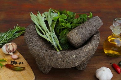 Photo of Mortar, different herbs, vegetables and oil on wooden table, closeup