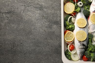 Photo of Raw fish with vegetables and lemon in baking dish on grey textured table, top view. Space for text