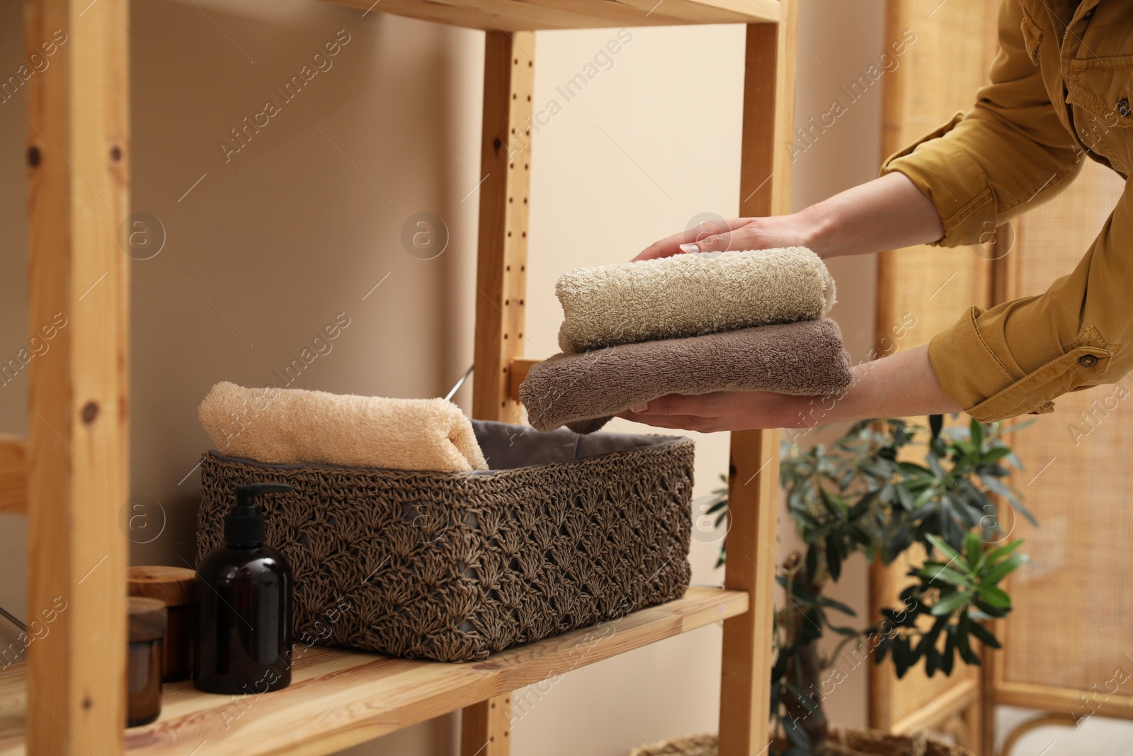 Photo of Woman putting towels into storage basket indoors, closeup