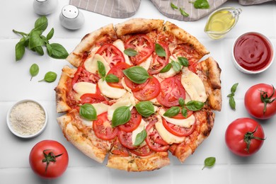 Photo of Delicious Caprese pizza and ingredients on white tiled table, flat lay