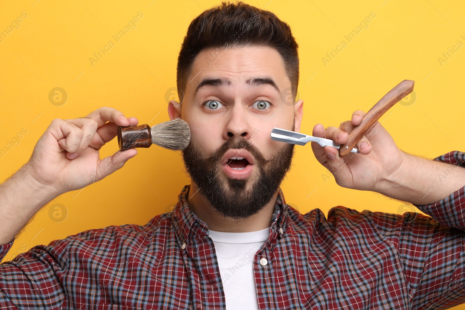 Photo of Handsome young man with mustache holding blade and shaving brush on yellow background