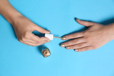 Woman applying nail polish on color background, top view