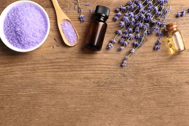 Photo of Bowl of sea salt, essential oil and lavender flowers on wooden table, flat lay. Space for text