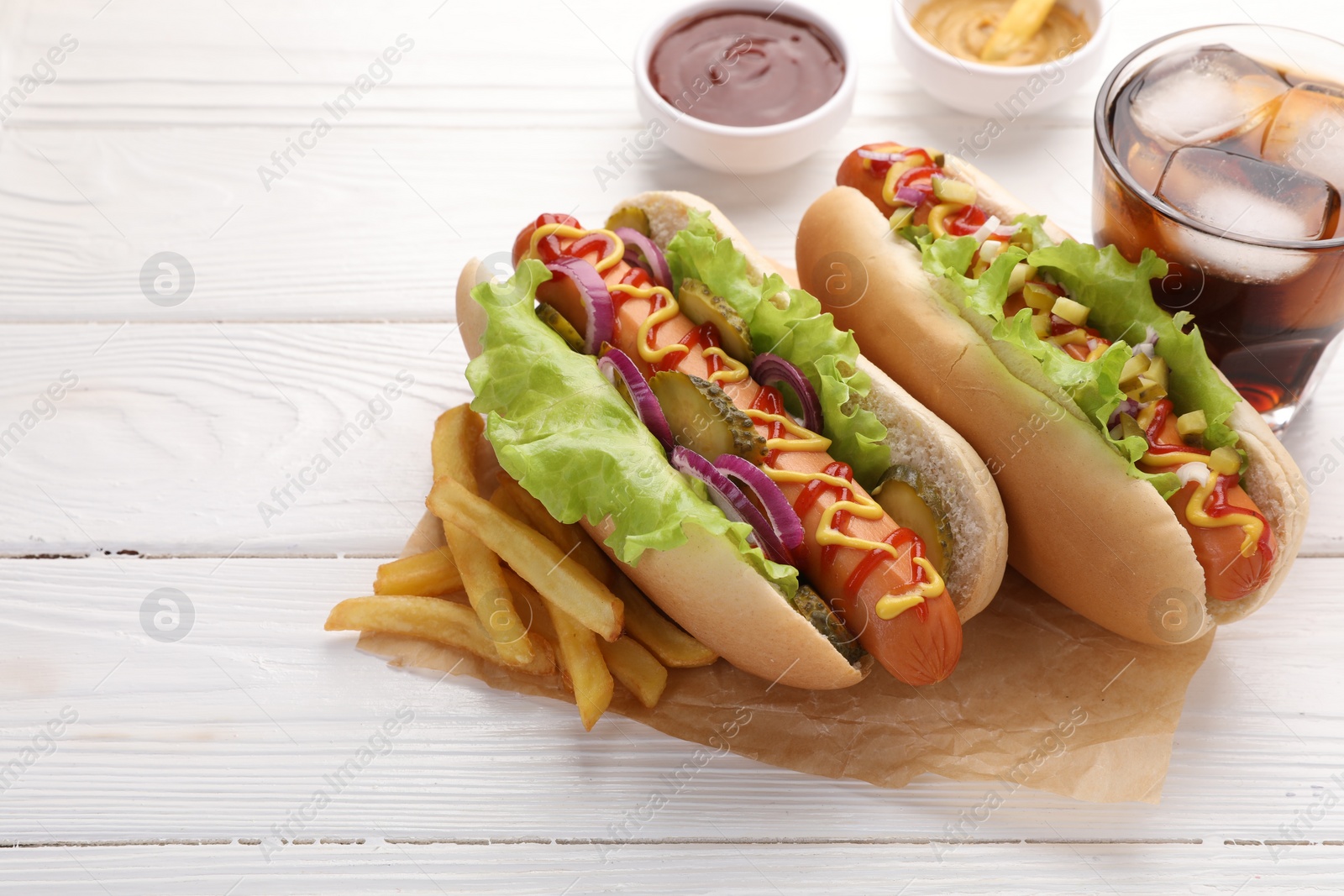 Photo of Delicious hot dogs with lettuce, onion and pickle served on white wooden table, closeup. Space for text