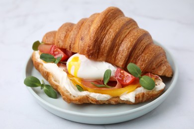 Tasty croissant with fried egg, tomato and microgreens on white table, closeup