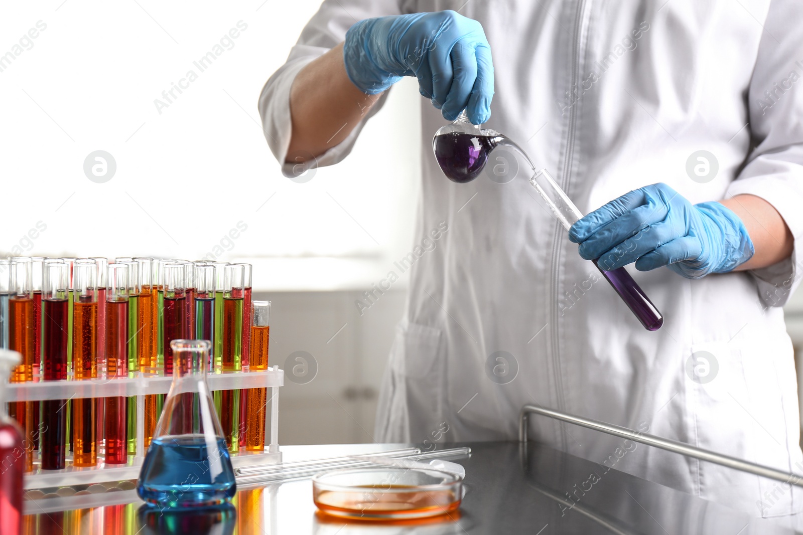 Photo of Scientist pouring liquid from retort flask into test tube at laboratory. Solution chemistry