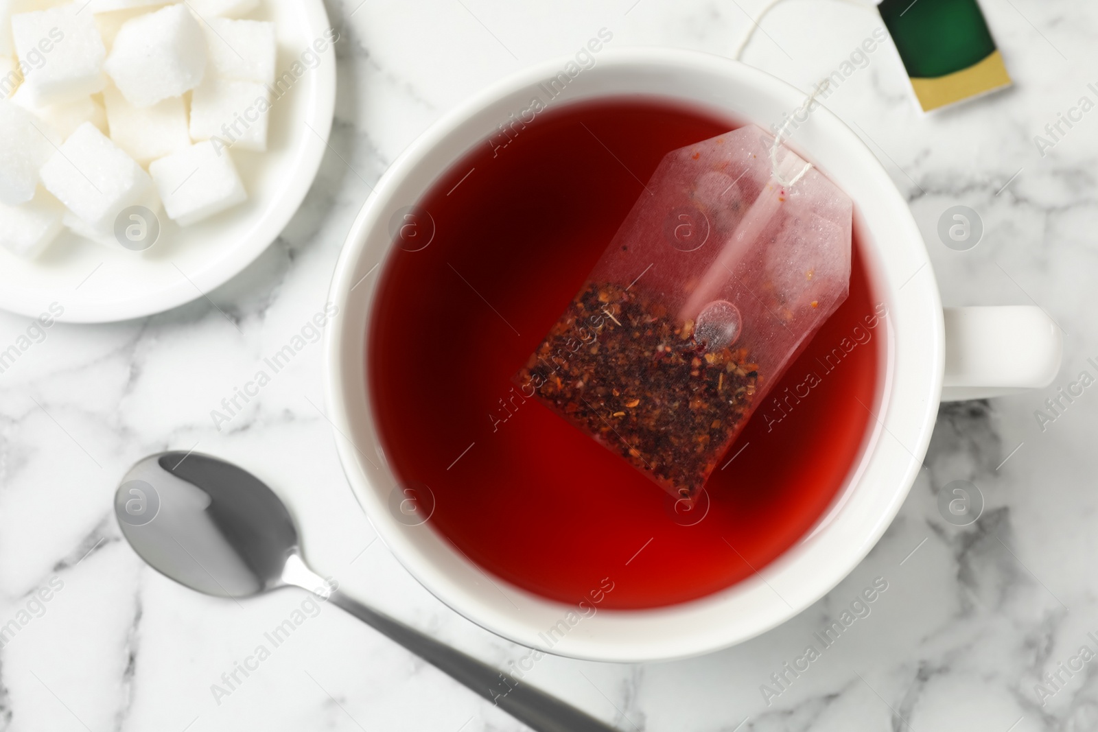 Photo of Tea bag in cup of hot water on white marble table, flat lay