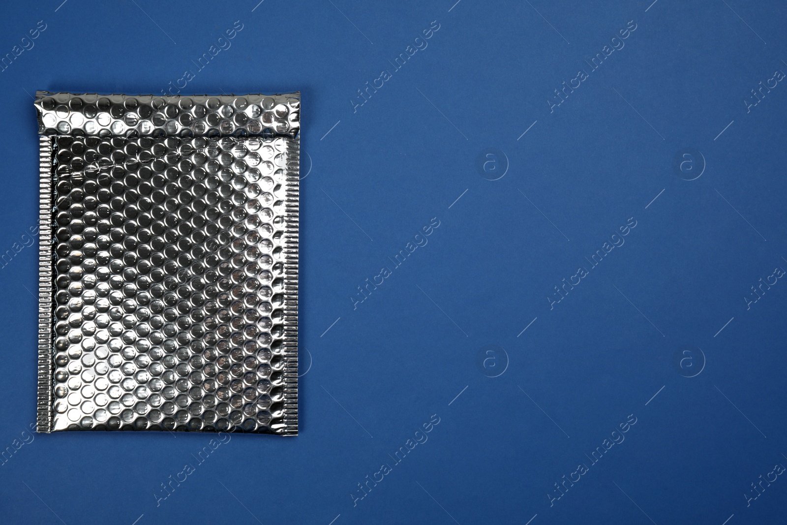 Photo of Padded envelope with bubble wrap on blue background, top view. Space for text