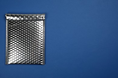 Padded envelope with bubble wrap on blue background, top view. Space for text