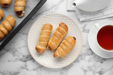 Photo of Delicious sausage rolls and hot drink on white marble table, flat lay