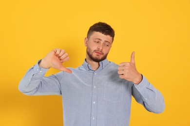 Photo of Young man showing thumbs up and down on orange background