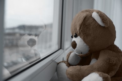 Photo of Cute lonely teddy bear on windowsill indoors, closeup. Space for text