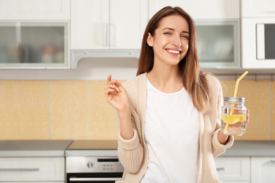 Photo of Young woman with mason jar of lemon water in kitchen