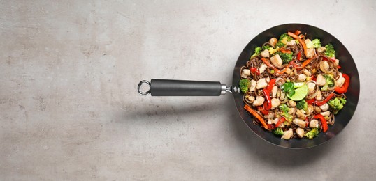 Photo of Stir-fry. Tasty noodles with meat and vegetables in wok on grey textured table, top view. Space for text