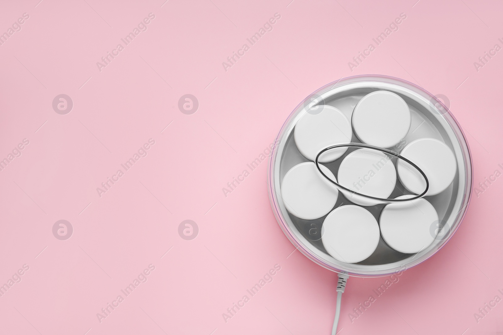 Photo of Modern yogurt maker with jars on pink background, top view. Space for text