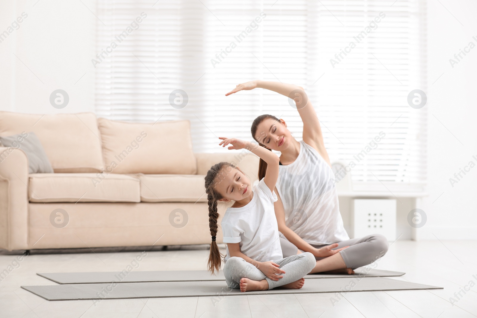 Photo of Young mother with little daughter practicing yoga at home