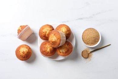 Photo of Delicious sweet muffins and brown sugar on white marble table, flat lay