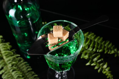 Photo of Absinthe in glass, brown sugar, spoon and green leaves on mirror table. Alcoholic drink