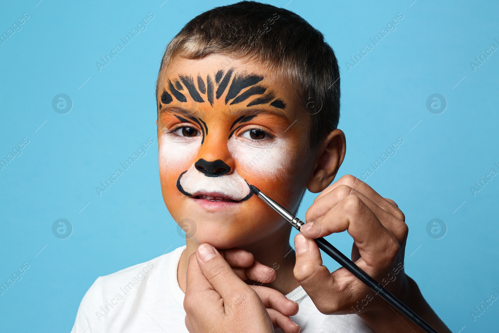 Photo of Artist painting face of little boy on blue background