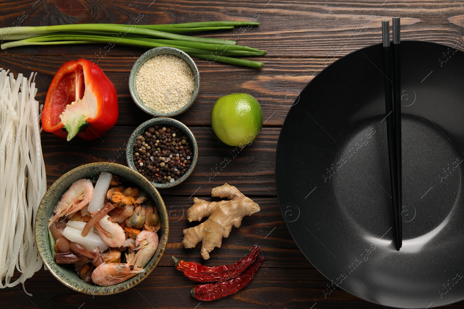 Photo of Black wok, chopsticks and products on wooden table, flat lay