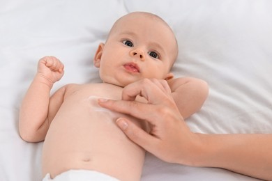 Woman applying body cream onto baby`s skin on bed, closeup