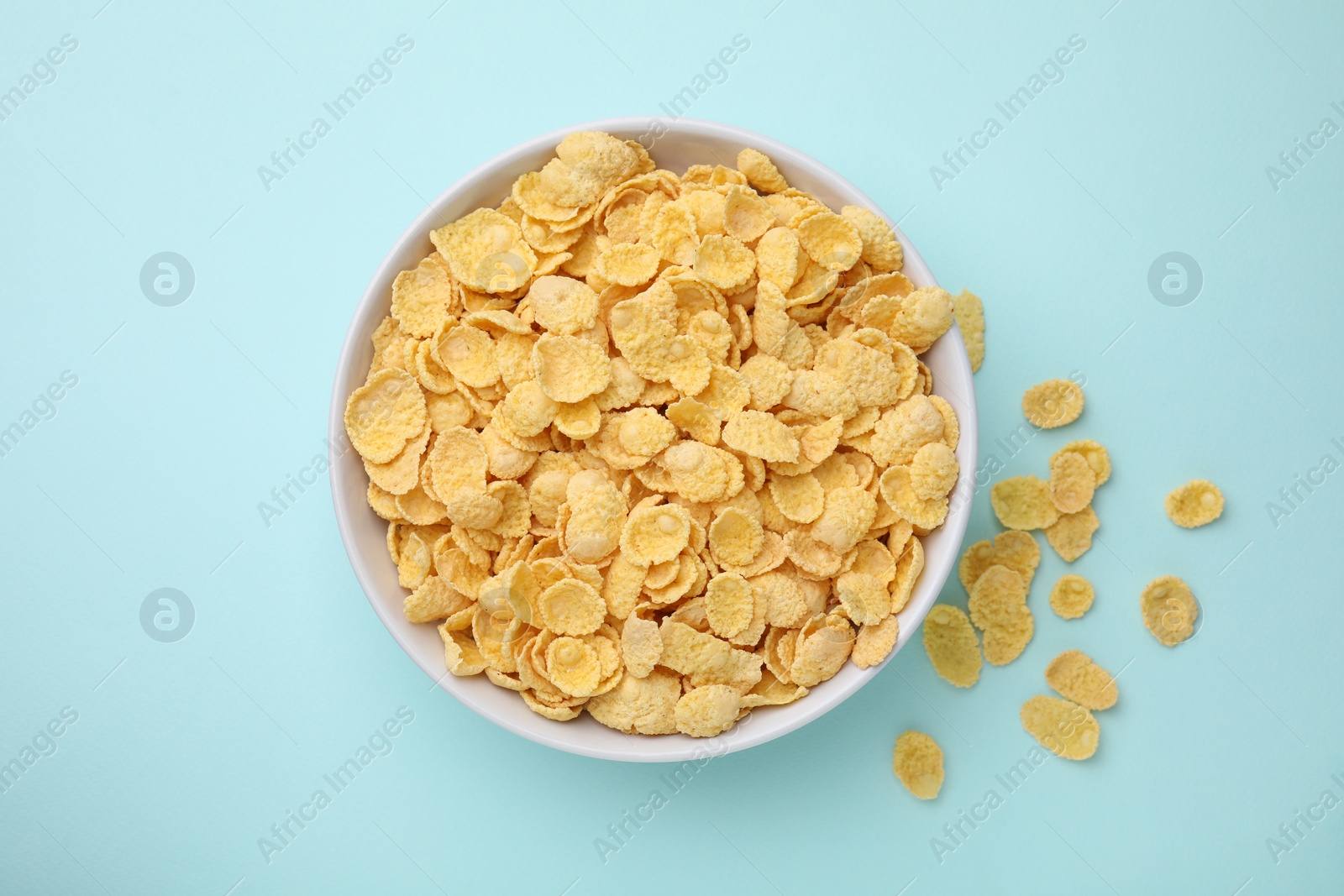 Photo of Breakfast cereal. Tasty corn flakes in bowl on light blue table, top view