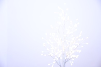 Decorative tree with lights on light background, blurred view. Space for text