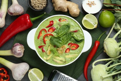 Photo of Saucepan with delicious green curry chicken soup and different ingredients on grey table, flat lay