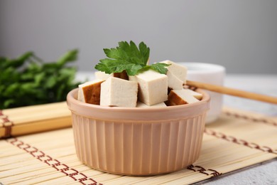 Photo of Bowl of smoked tofu cubes and parsley on bamboo mat, closeup