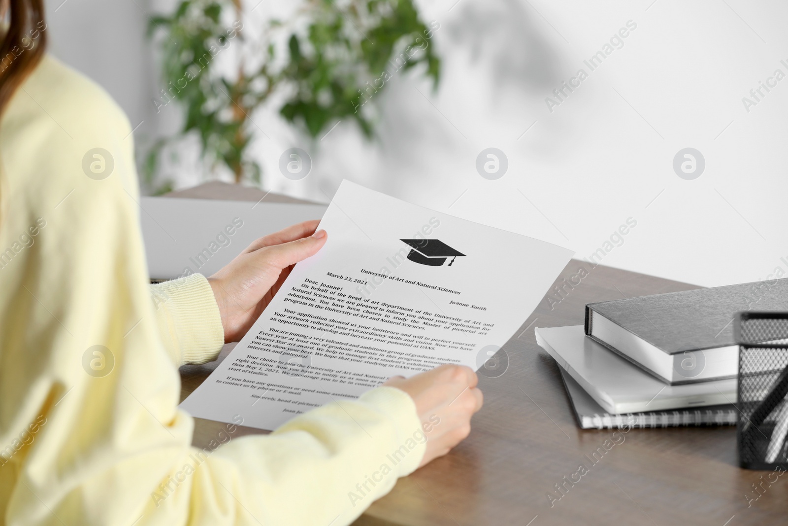 Photo of Student with acceptance letter from university at wooden table indoors, closeup