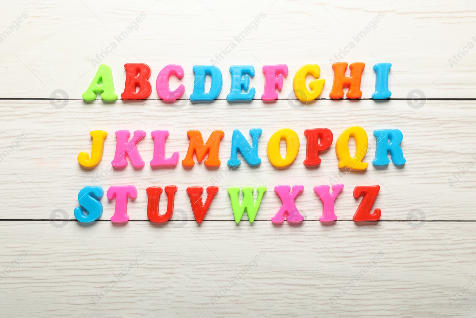 Photo of Colorful magnetic letters on white wooden table, flat lay. Alphabetical order