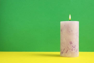 Alight wax candle on color background. Space for text