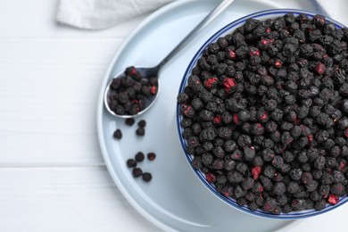 Bowl and spoon with dried blueberries on white wooden table, top view