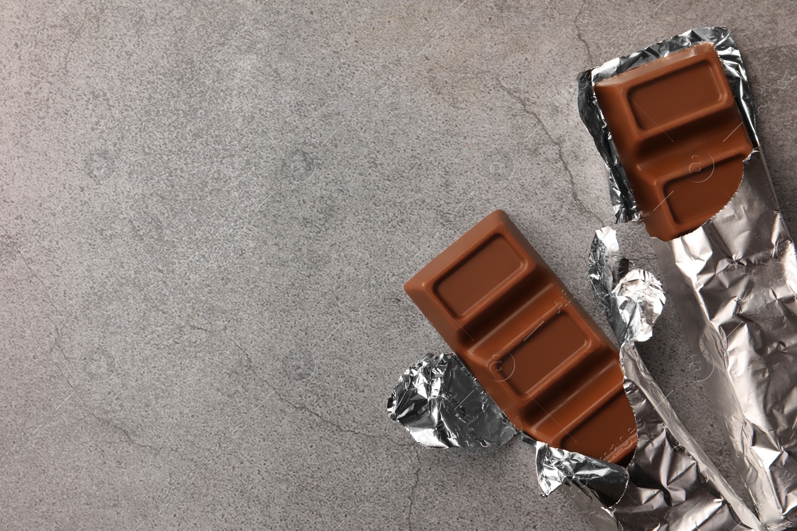 Photo of Tasty chocolate bars wrapped in foil on grey table, flat lay. Space for text