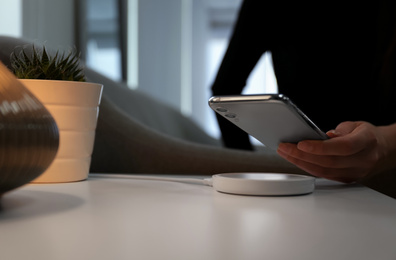 Woman putting smartphone on wireless charger in room, closeup