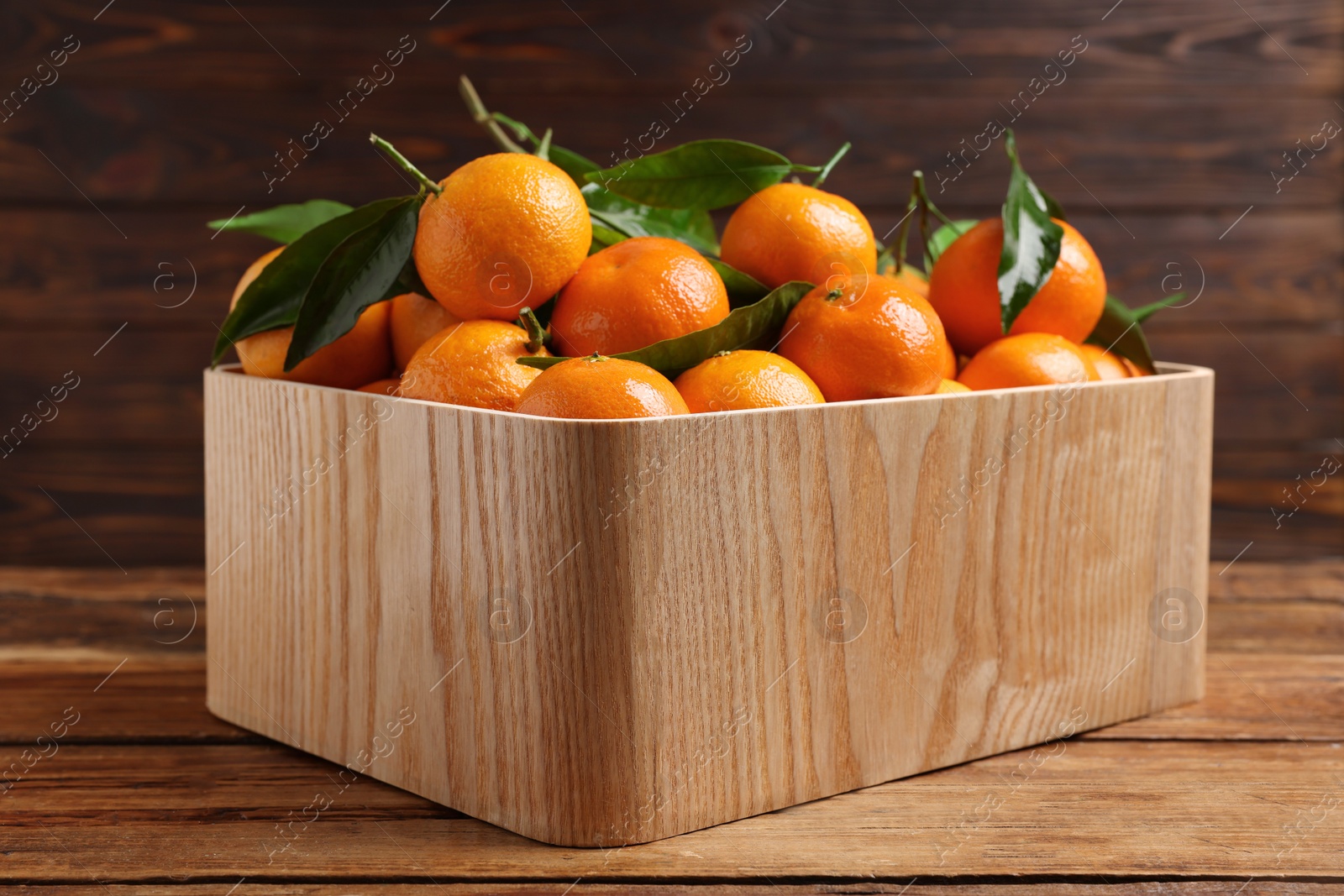 Photo of Fresh tangerines with green leaves in crate on wooden table