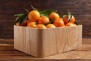 Fresh tangerines with green leaves in crate on wooden table