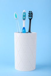 Photo of Different toothbrushes in holder on light blue background
