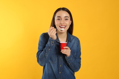 Photo of Portrait of happy woman eating tasty yogurt on orange background