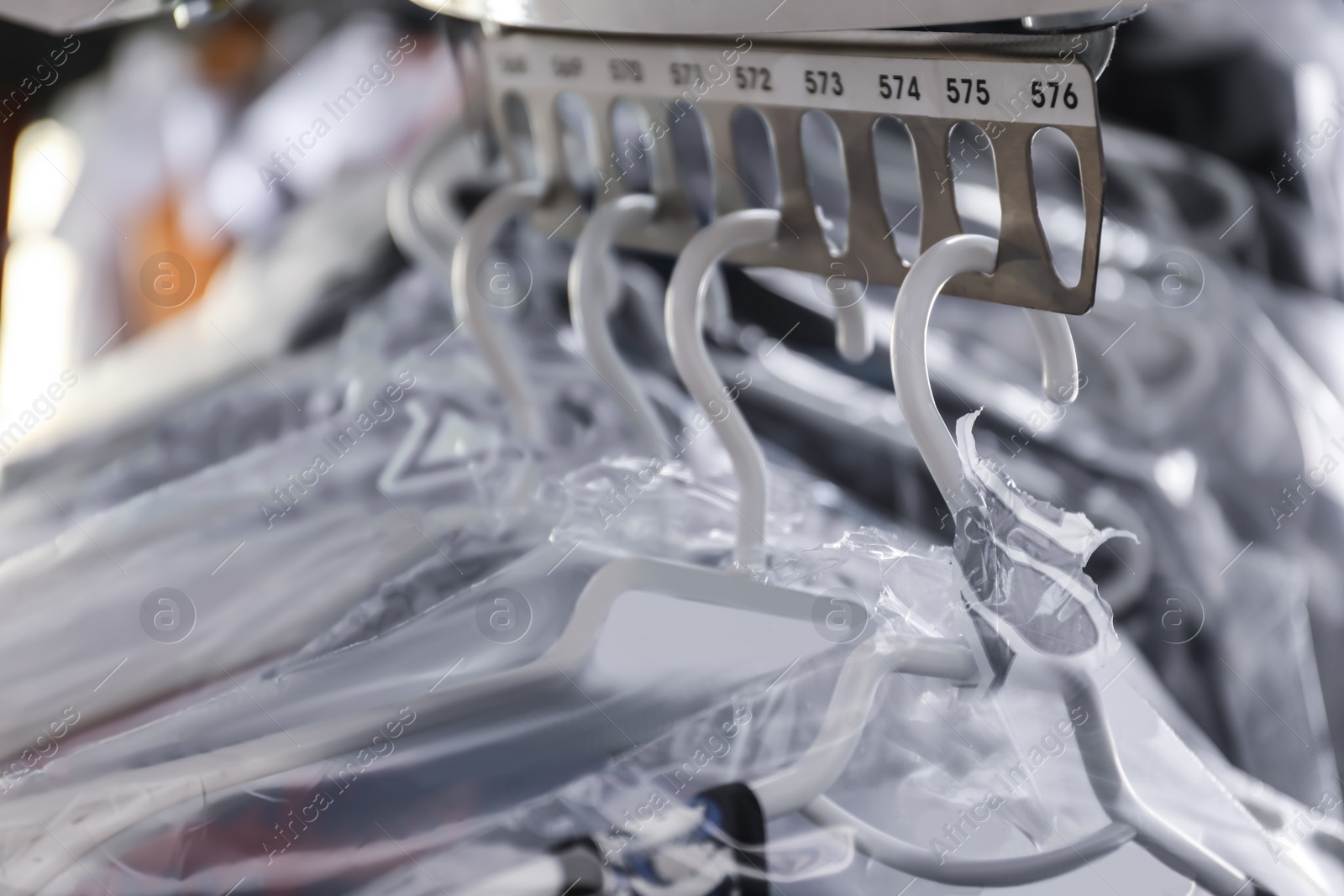 Photo of Hangers with clothes on garment conveyor at dry-cleaner's, closeup