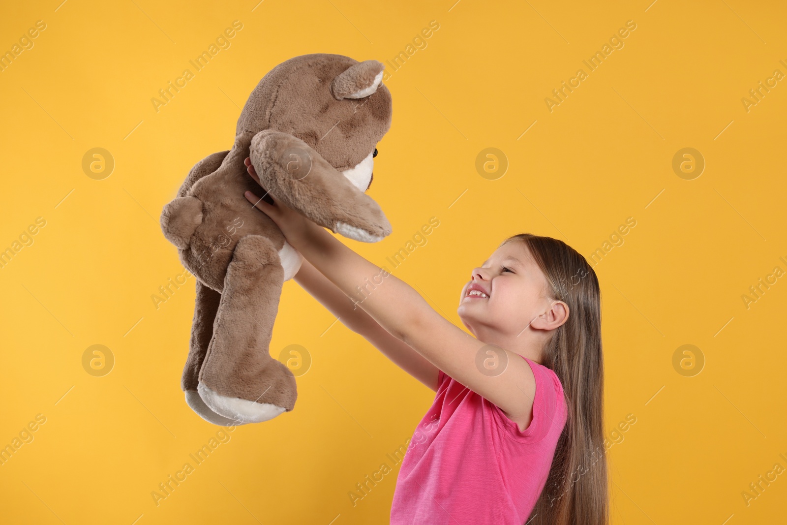 Photo of Cute little girl with teddy bear on yellow background