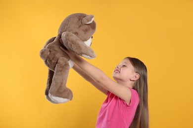 Photo of Cute little girl with teddy bear on yellow background