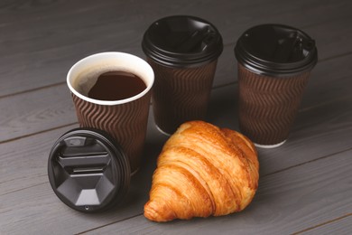 Photo of Coffee to go. Paper cups with tasty drink and croissant on grey wooden table