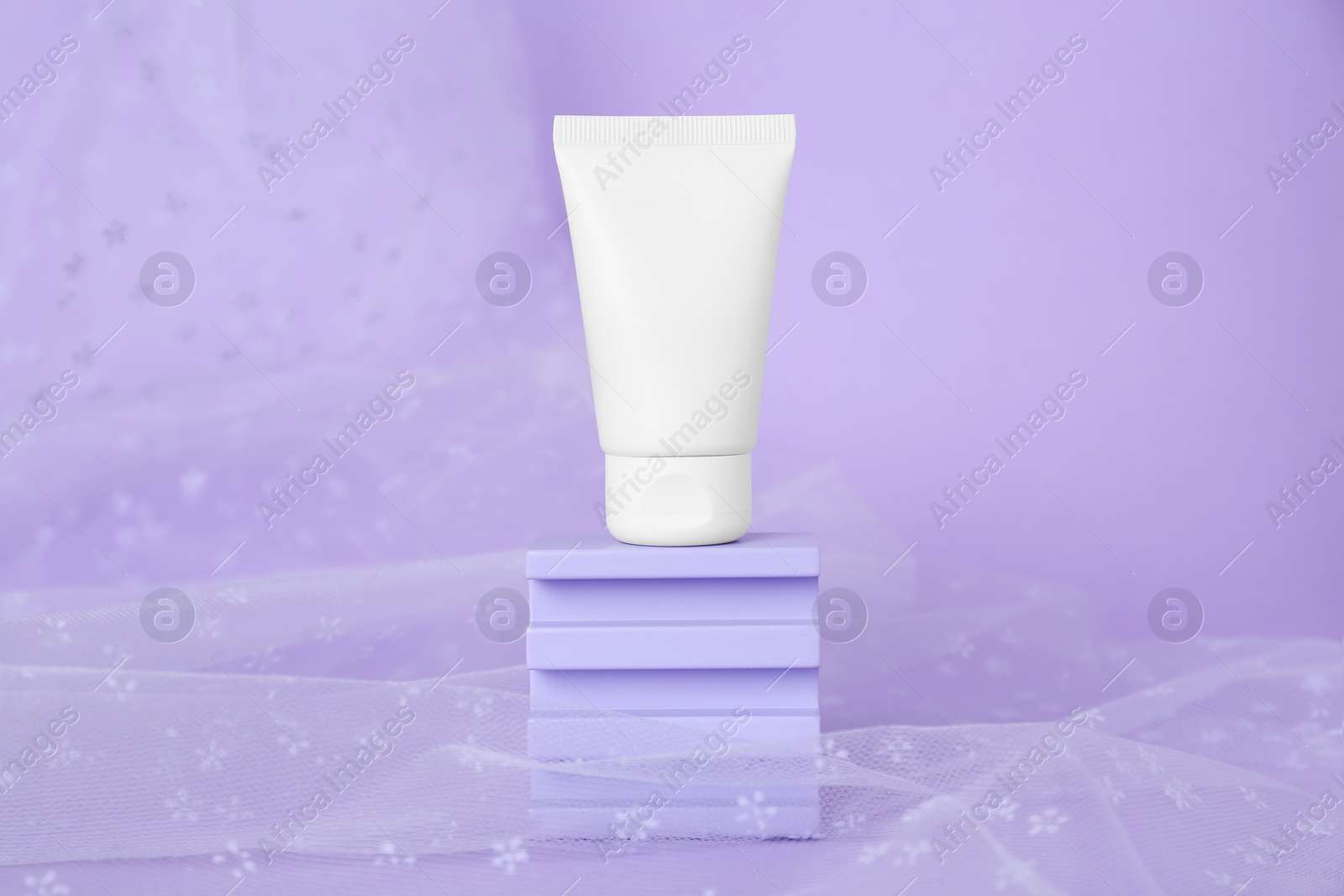 Photo of Tube of hand cream and fabric on violet background