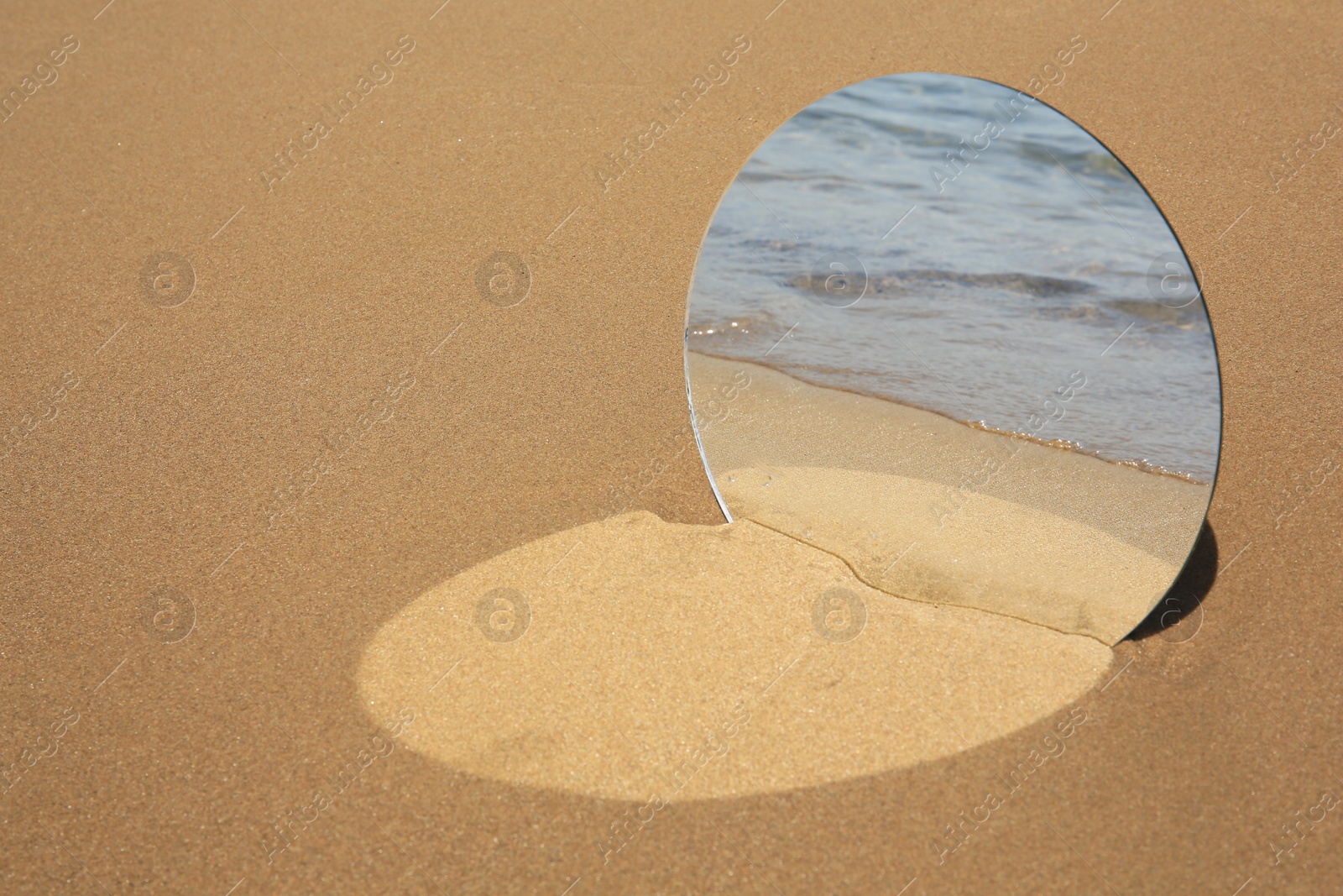 Photo of Round mirror reflecting sea on sandy beach, space for text