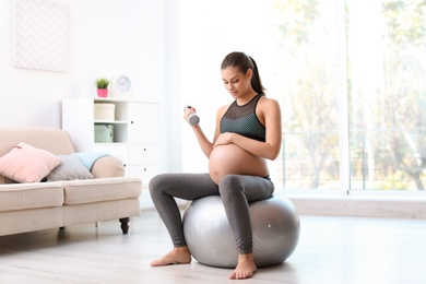 Photo of Young pregnant woman in fitness clothes lifting dumbbell at home