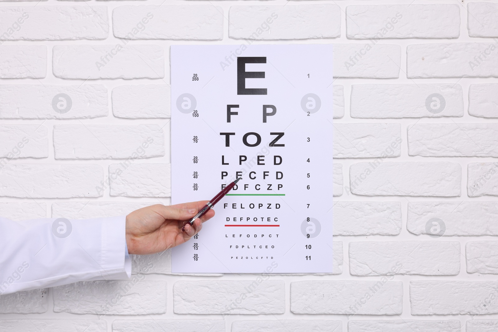 Photo of Ophthalmologist pointing at vision test chart on white brick wall, closeup