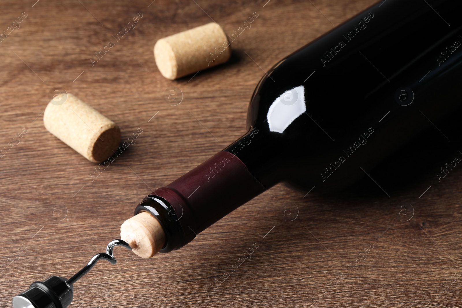 Photo of Opening wine bottle with corkscrew on wooden table, closeup